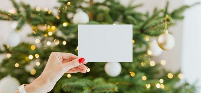 Eleganckie kartki bożonarodzeniowe dla firm leżące na drewnianym stole obok choinkowych ozdób